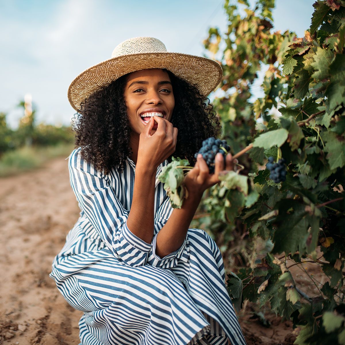 Young black woman eating a grape in a vineyard