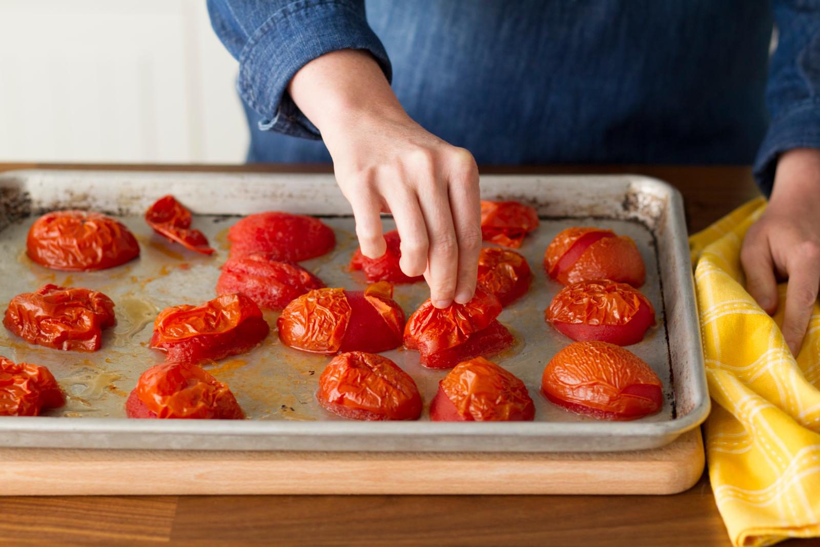 roasted halved tomatoes on sheet ban hand removing skin