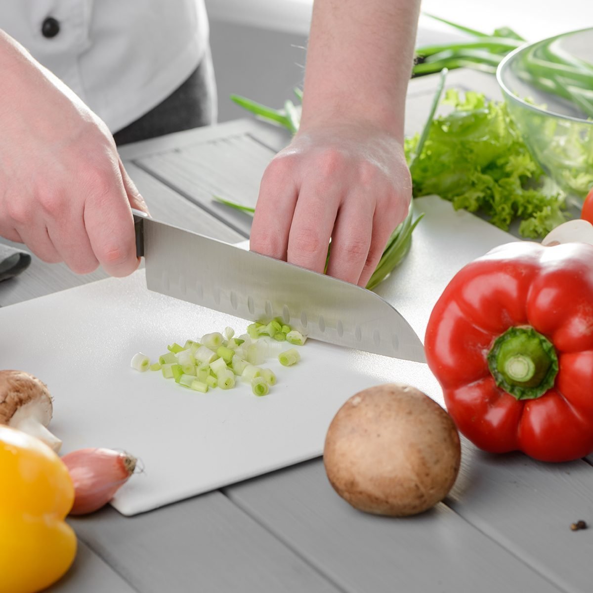 Chef cook chopping spring onions on a white board.