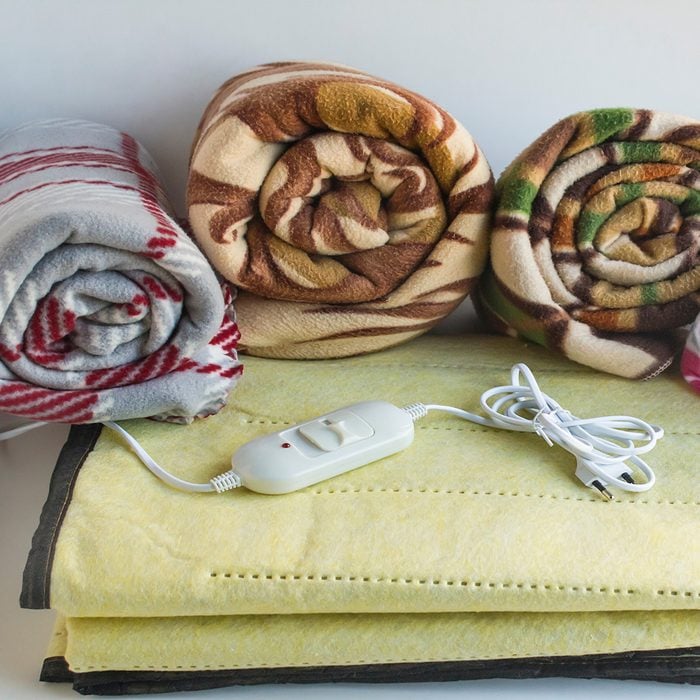 Four different size and color fleece blanket rolled on electric blanket.