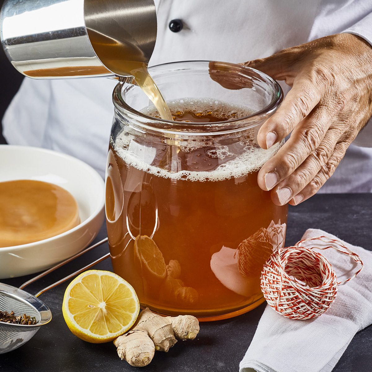 Man pouring a brew of sweetened black tea into a sterilised glass jar ready to add the scoby while making homemade kombucha