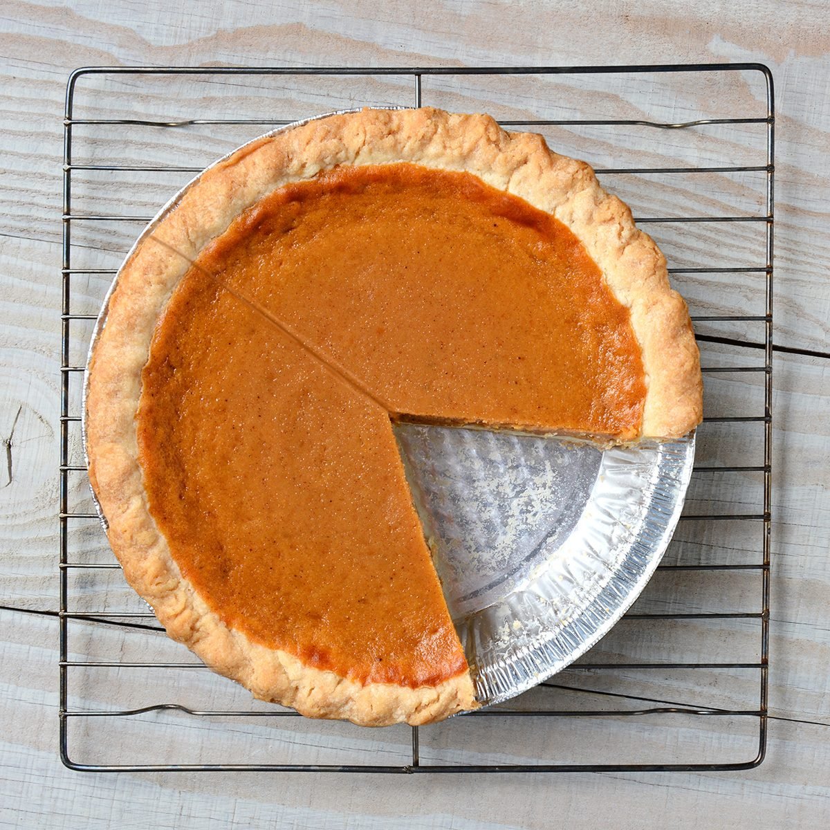 Overhead shot of a pumpkin pie with a slice cut out on a cooling rack. Horizontal format on a rustic white kitchen table.; Shutterstock ID 268798316; Job (TFH, TOH, RD, BNB, CWM, CM): TOH