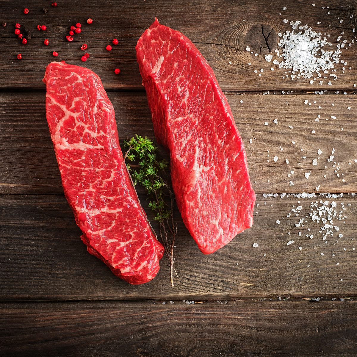two denver cut steaks on wood table with seasonings