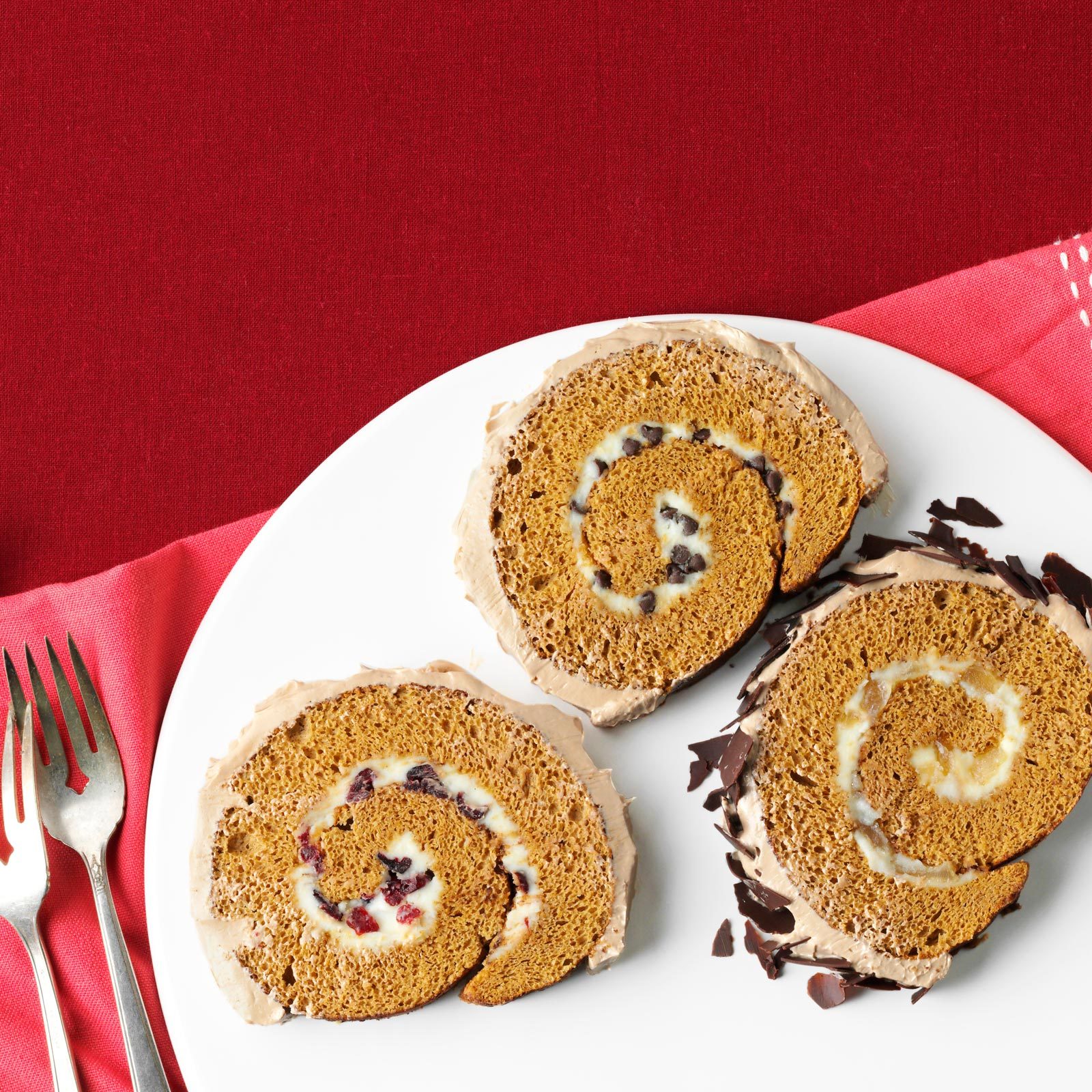 three slices of a Yule log cake slices on a white plate with a red background