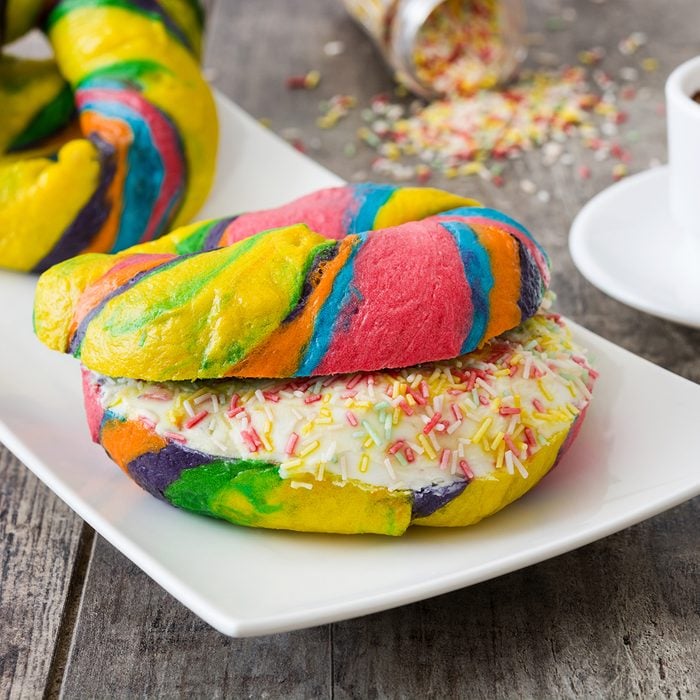 Colorful bagels with cheese and sprinkles and coffee on a wooden table