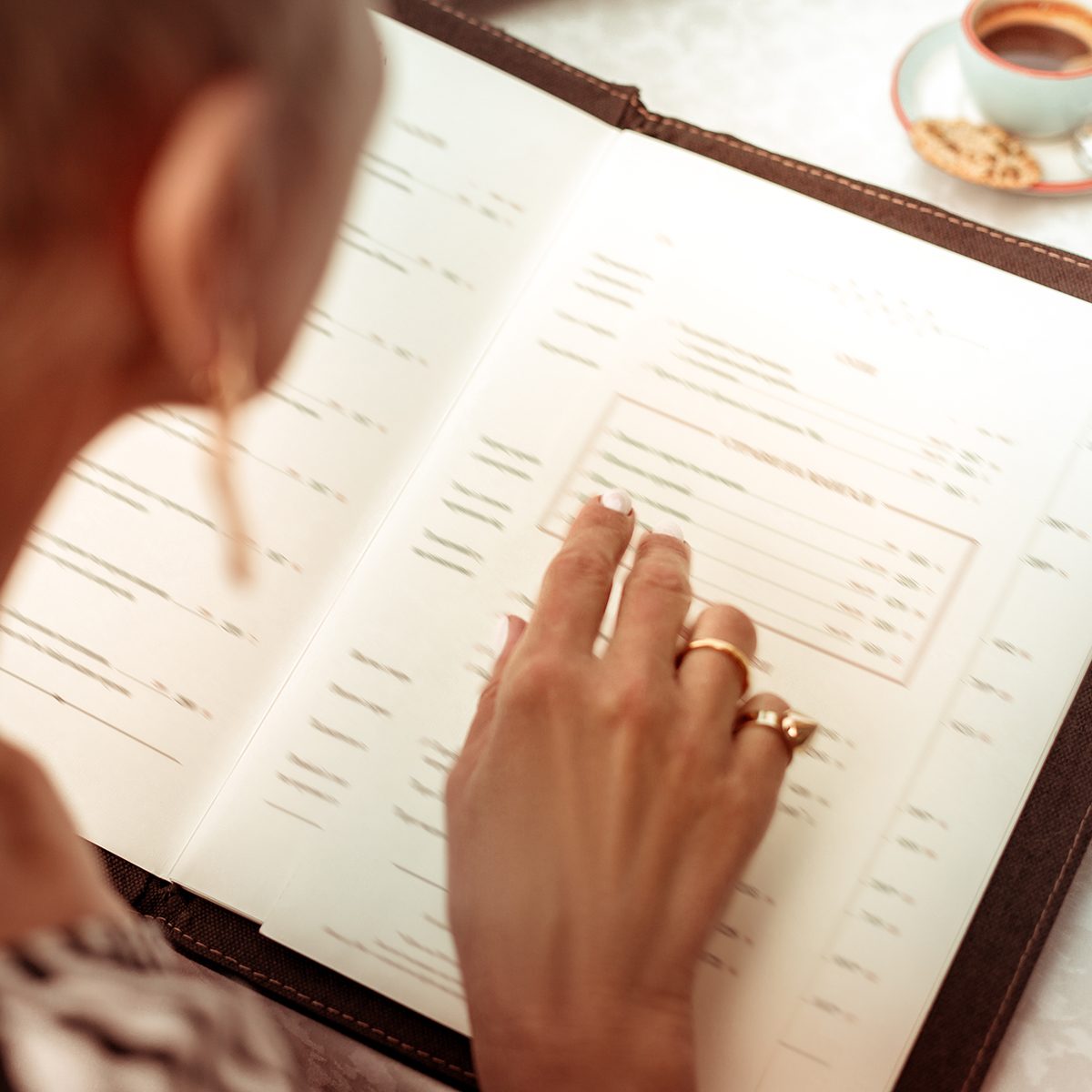 Reading the menu. Top view of woman wearing nice rings reading the menu in restaurant sitting at summer terrace