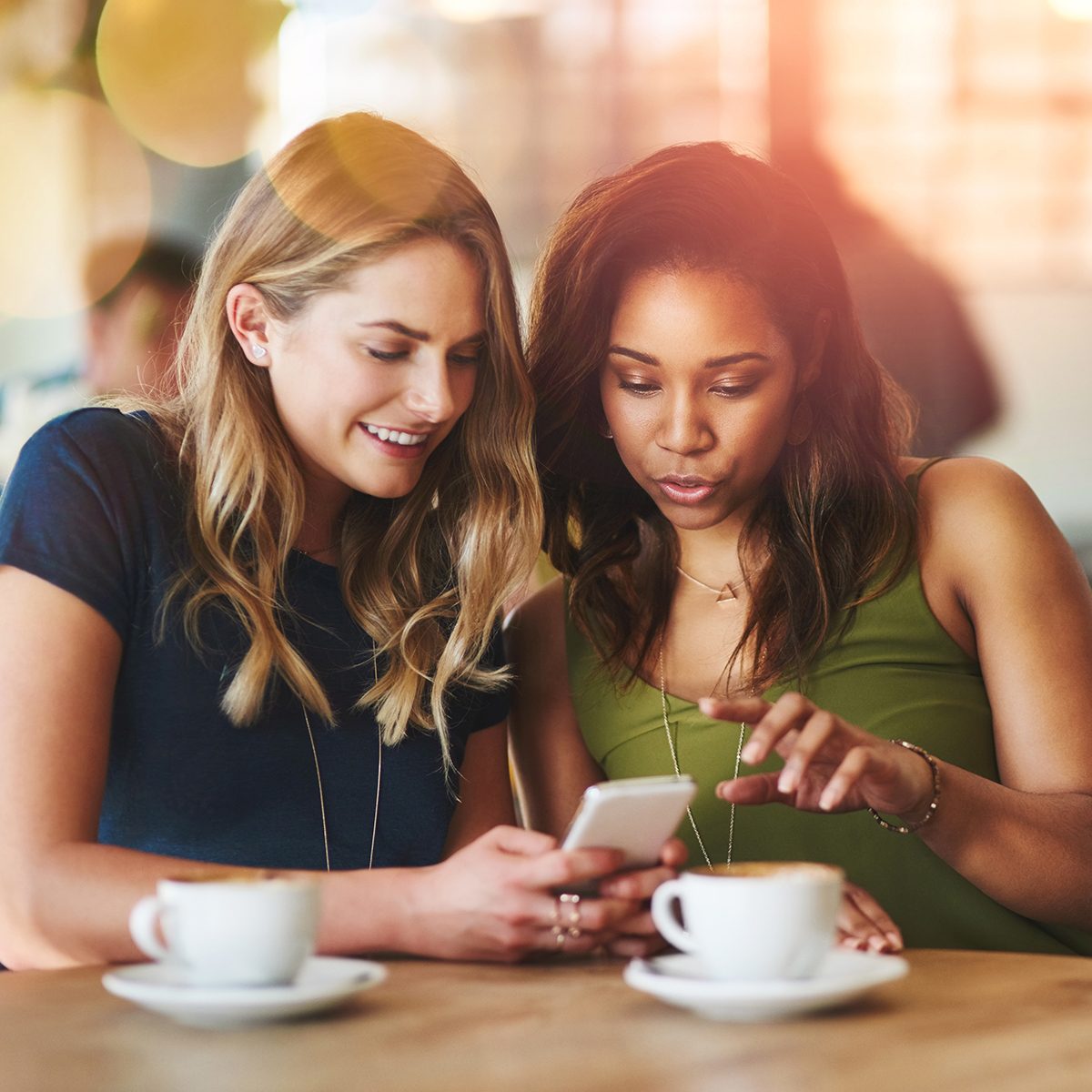 Cropped shot of girlfriends sharing something on a cellphone while sitting in a cafe