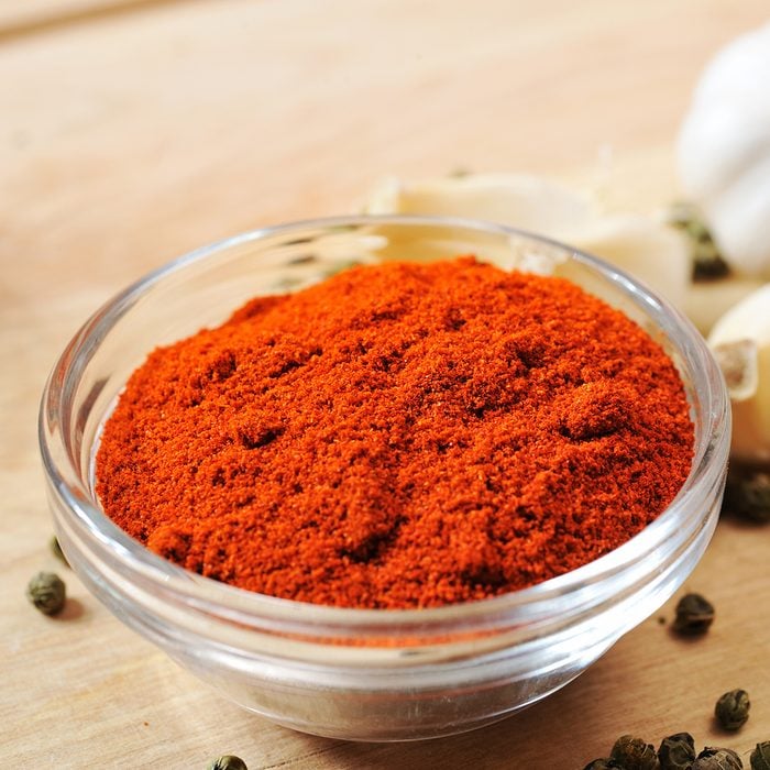close up of ground paprika in the glass dish on the table with few pepper seeds and garlic pieces aroundsee other similar images: