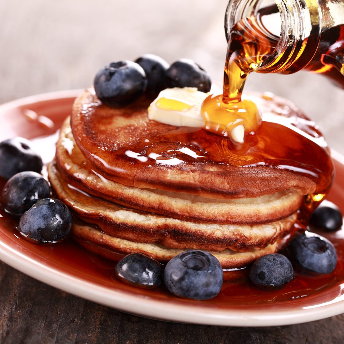 Pouring maple syrup on stack of pancakes