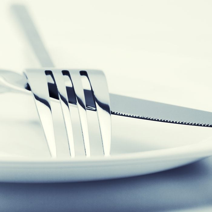 White plate, fork and knife on light background. Toned image.