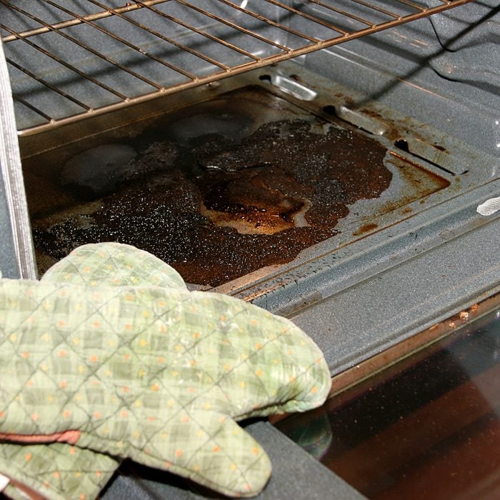 Badly burnt oven with oven mits in forefront