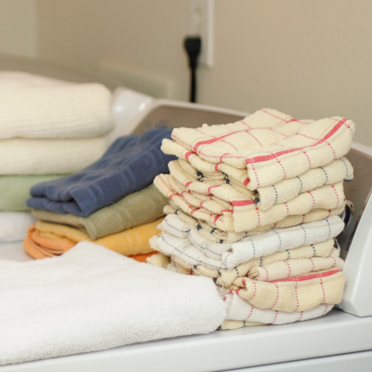 Arms and hands of a male folding towels onto a dryer and washer in a laundry room..