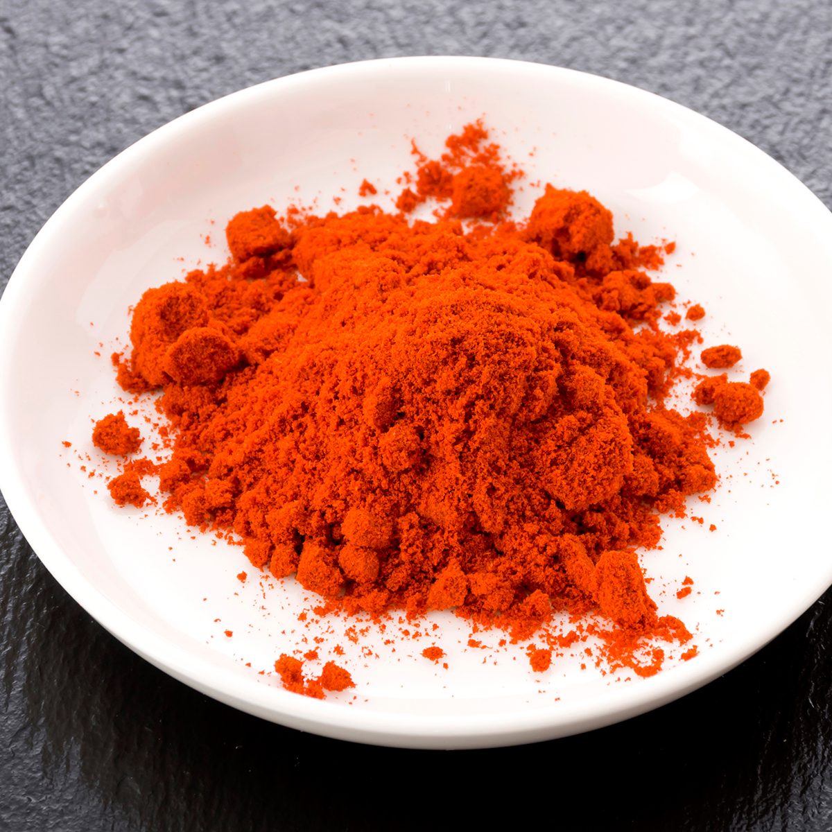 Paprika powder on a white plate on black stone background