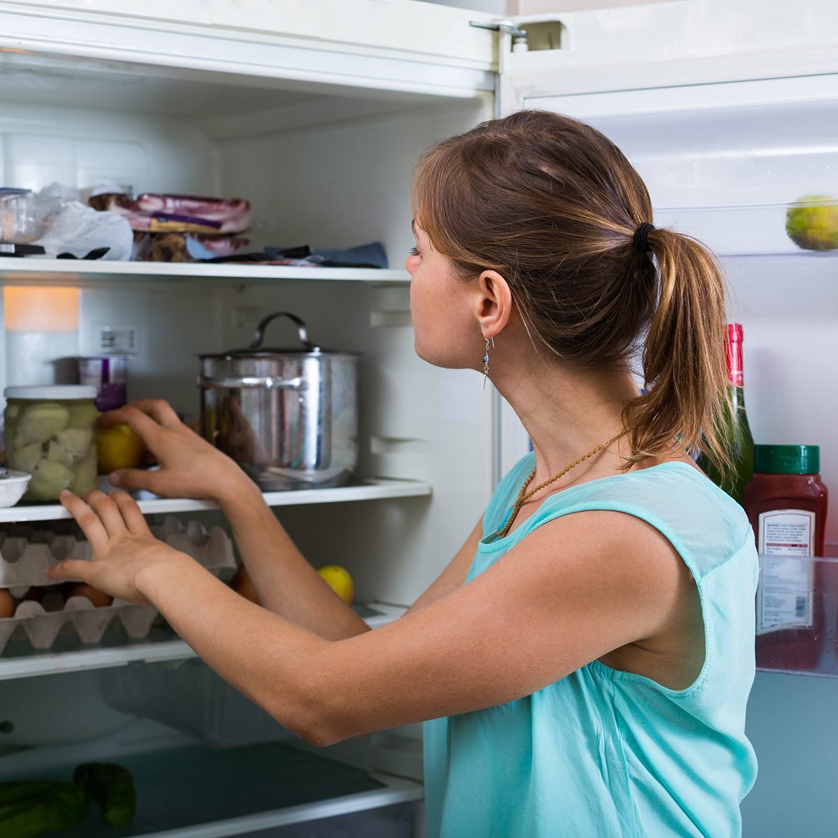 Young woman standing near refrigerator filled with products