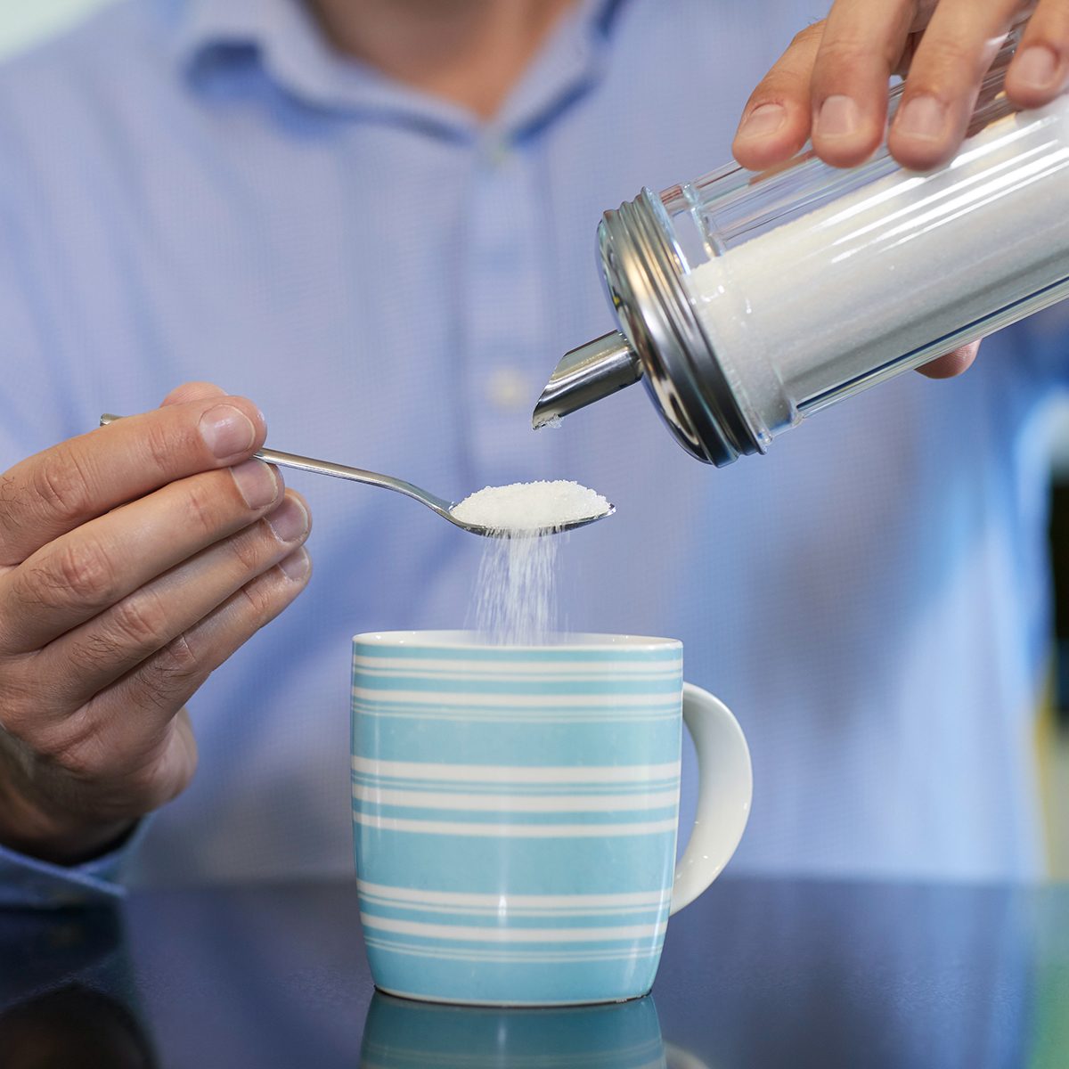 Close Up Of Mature Man Adding Sugar To Hot Drink At Home