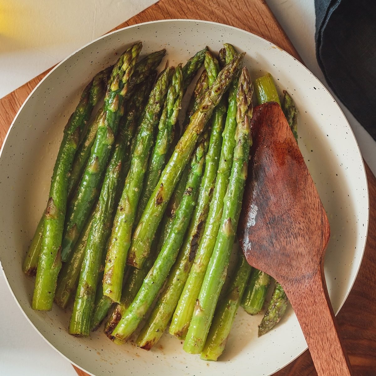 Top view on roasted asparagus in a white pan on a kitchen table. Modern style, vegetarian food.