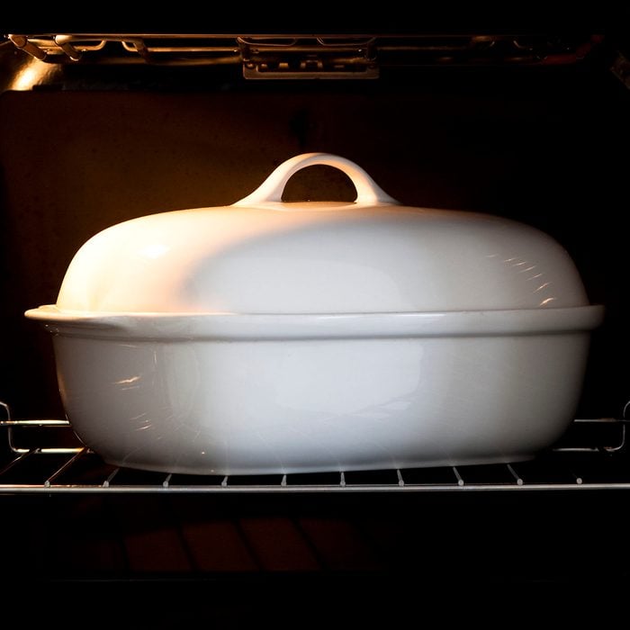 White porcelain baking dish with lid in open oven with light switch on
