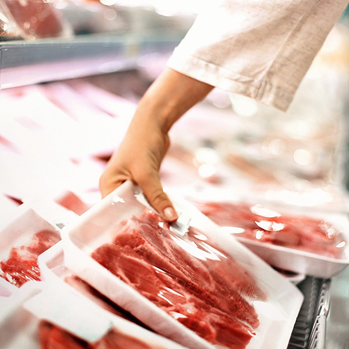 Closeup side view of unrecognizable woman chossing some fresh meat at local supermarket. The meat is cut into chops and packed into one pound packages. She has reached for a package of beef sirloin steaks.