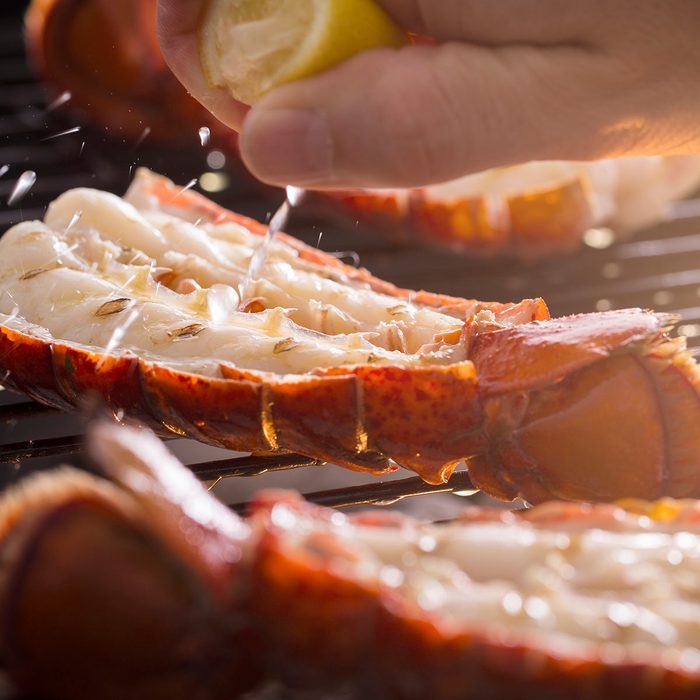 Fresh cold water lobster tails being cooked on a outdoor grill with fresh lemon juice being squeezed on the tails.