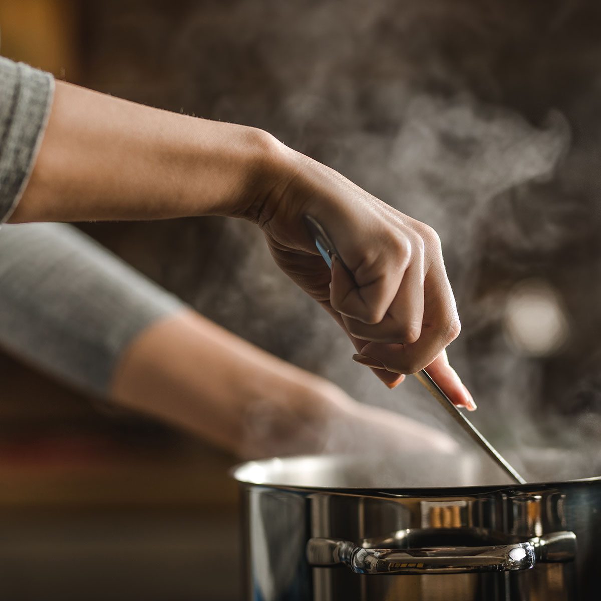 Unrecognizable woman making lunch in the kitchen and stirring soup.