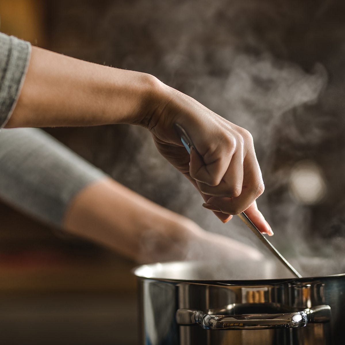 Unrecognizable woman making lunch in the kitchen and stirring soup.