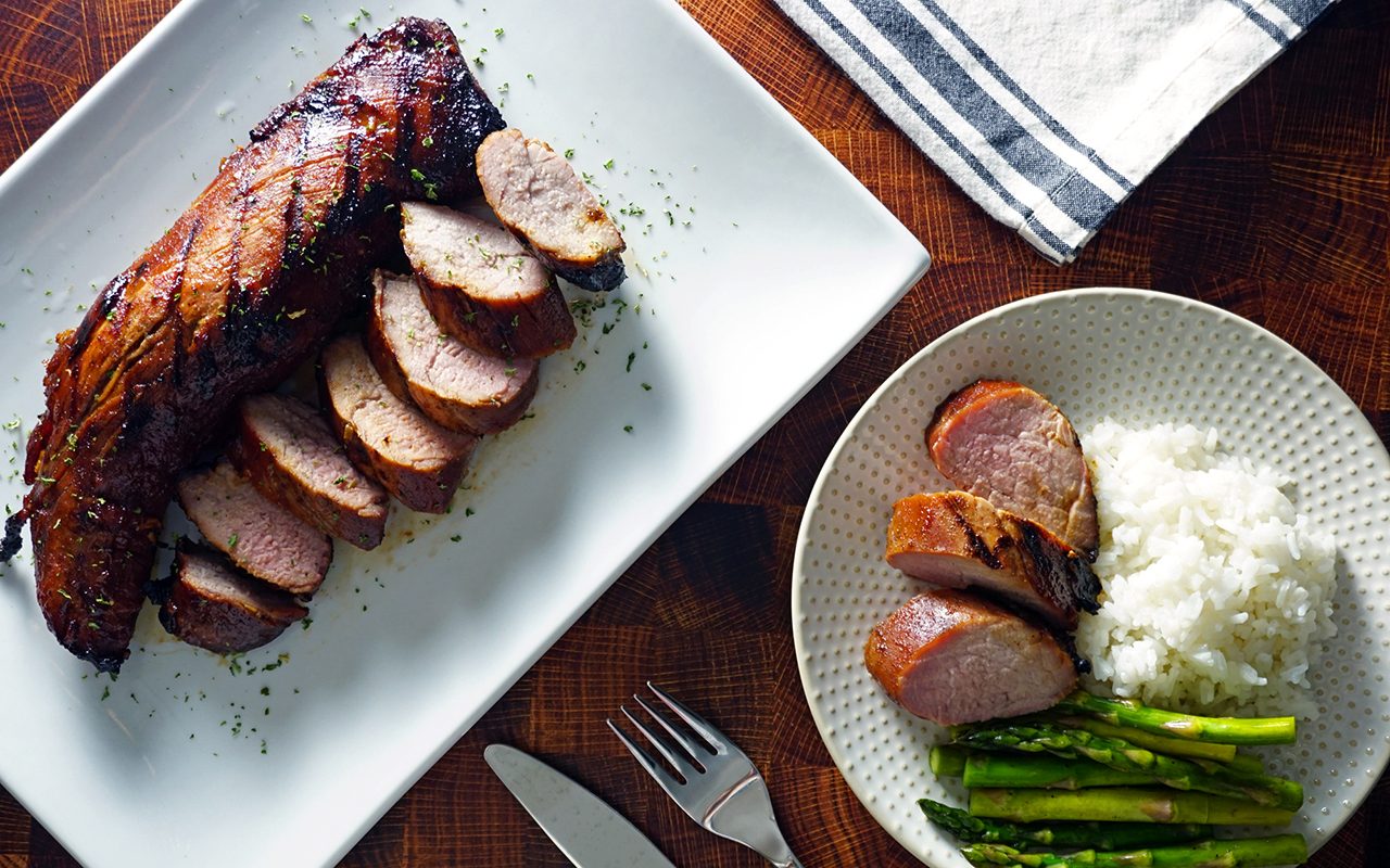 teriyaki grilled pork tenderloin served on a platter and plated with rice and grilled aparagus