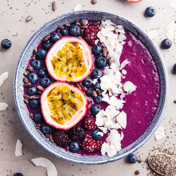 Tasty appetizing smoothie acai bowl made from blackberries and wild berries, decorated with cut passion fruit, coconut flakes, and cacao nibs. Served in bowl. Healthy life clean eating concept.