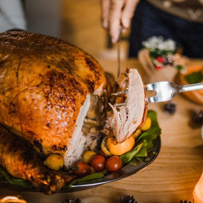 Close up of unrecognizable person carving white meat during dinner at dining table.