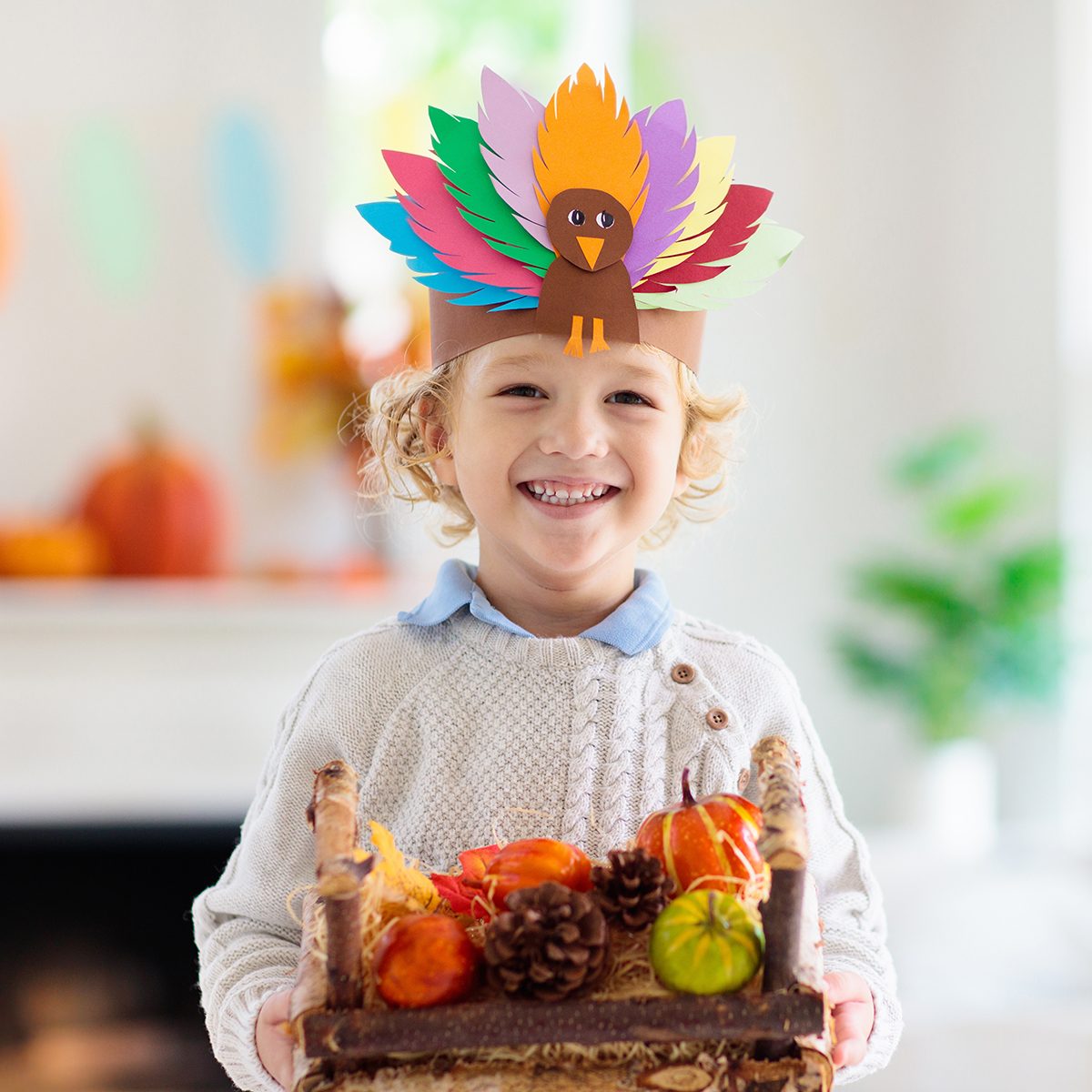 Child celebrating Thanksgiving. Kid holding pumpkin in paper turkey hat. Autumn fun crafts and art. Little blond curly boy in decorated living room. Warm knitted wear. Fall season decoration.