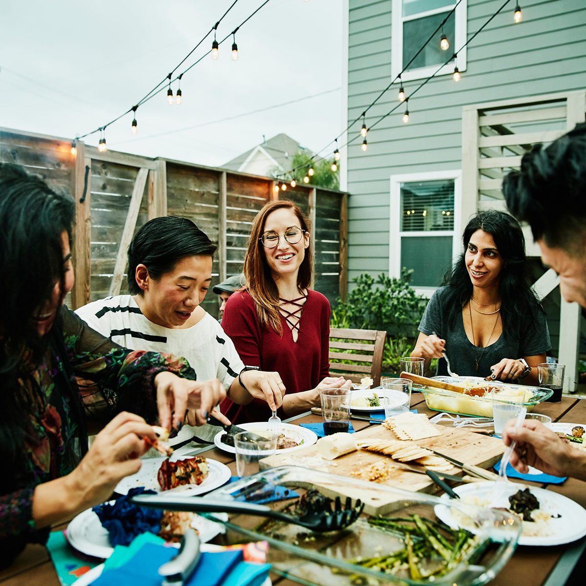 Smiling and laughing friends sharing dinner at table in backyard