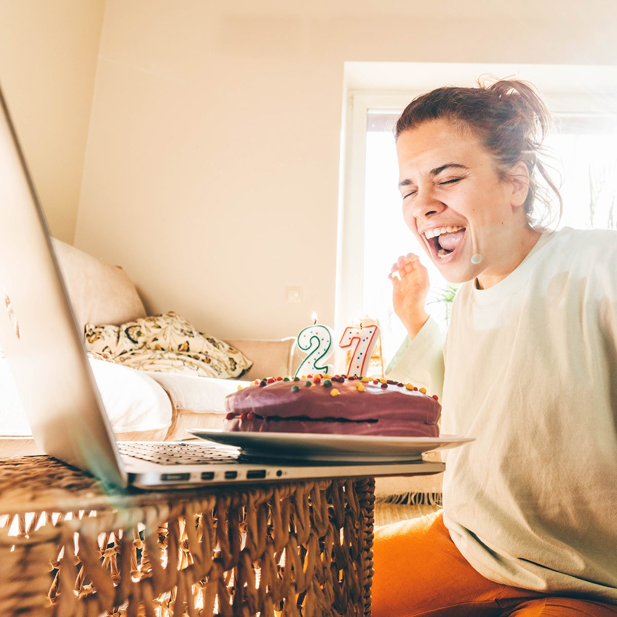 Woman blowing out the candle on the birthday cake and making video call. Girl celebrating birthday online in quarantine time.