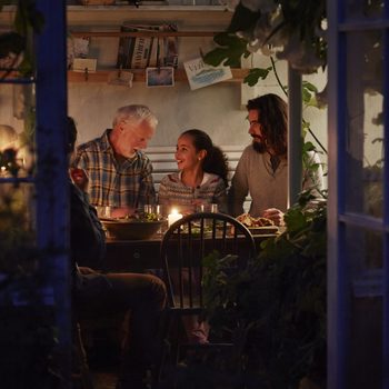 Family Around a Table by Candlelight, Enjoying Food to Eat When the Power Is Out