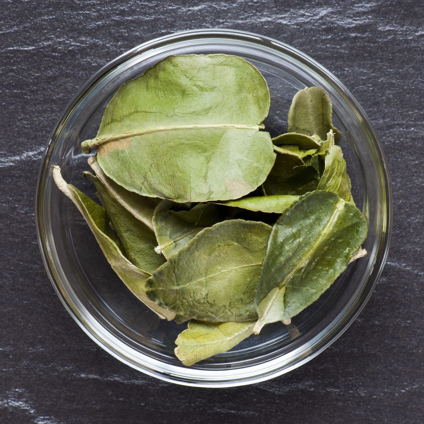 dried Makrut Lime Leaves in a small glass bowl on dark counter
