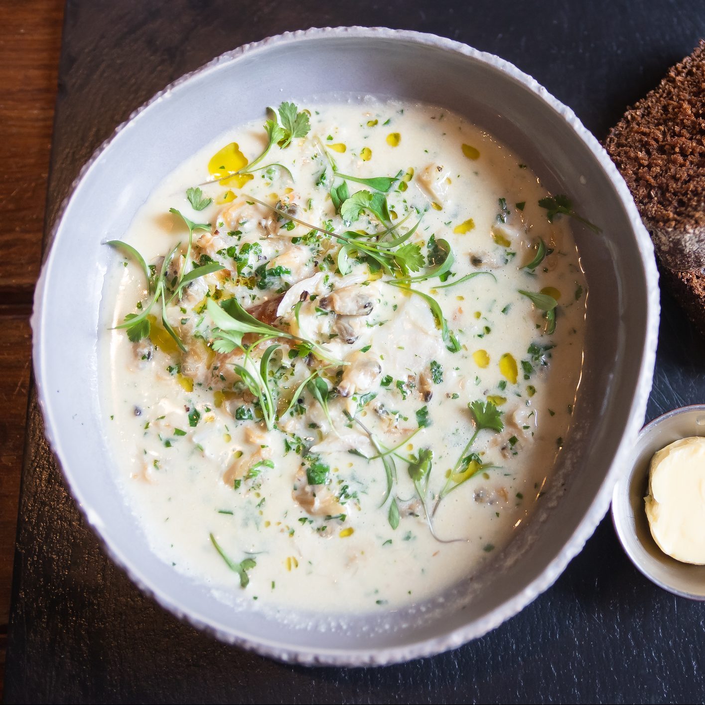 seafood chowder, corn bread and butter in a bowl on a black board