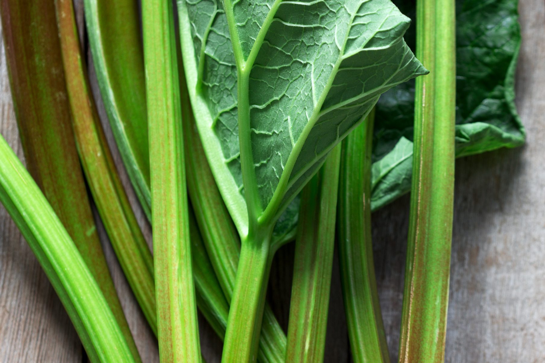 Stems and leaves of rhubarb on a wooden background.