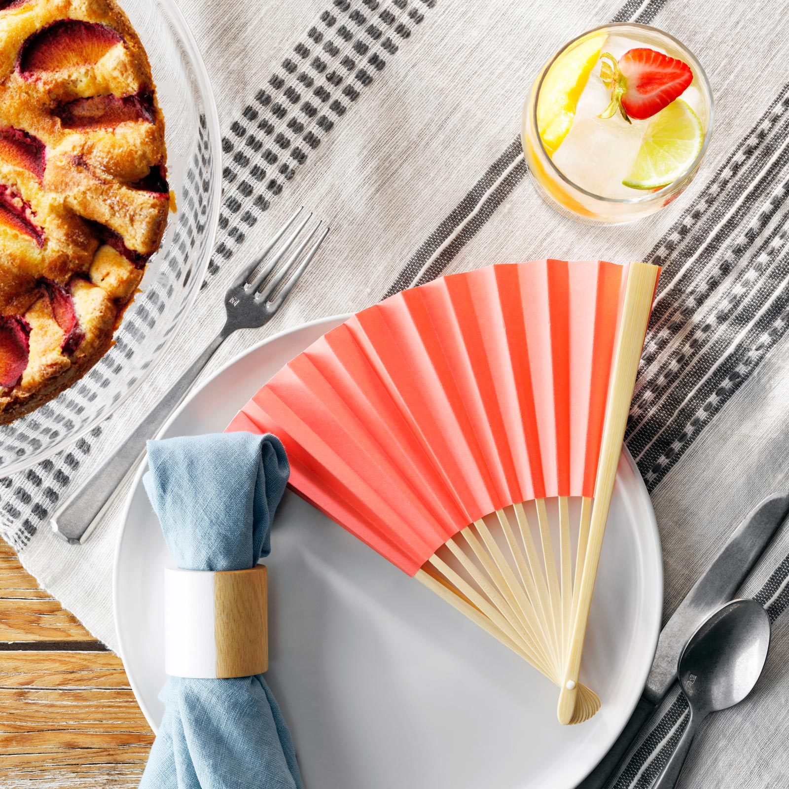 outdoor party place setting with a pink paper fan and blue cloth napkin on a plate