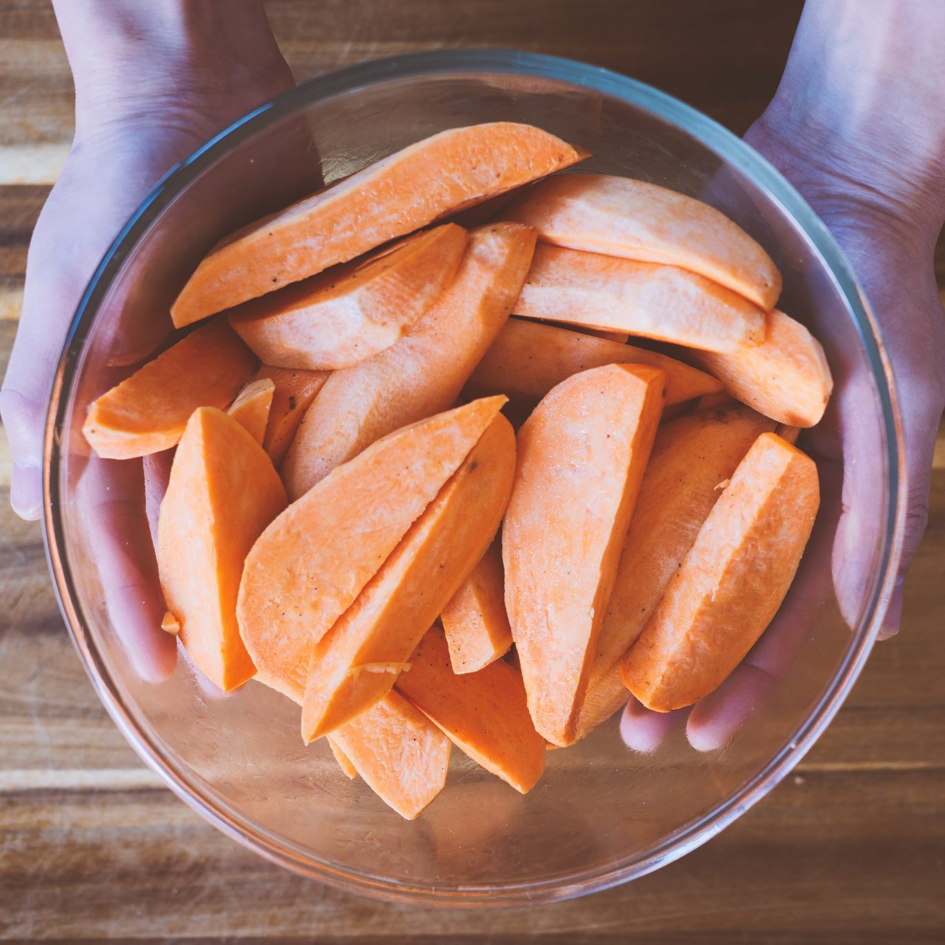 hand holding bowl of raw sweet potato wedges