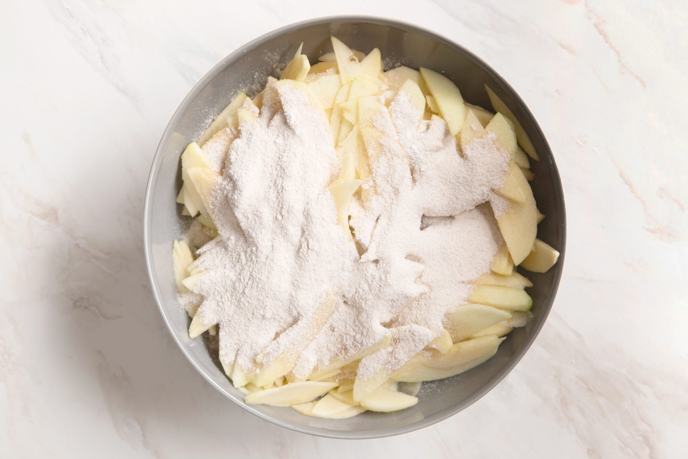 tossing apples with the cinnamon sugar mixture on a bowl on a kitchen counter