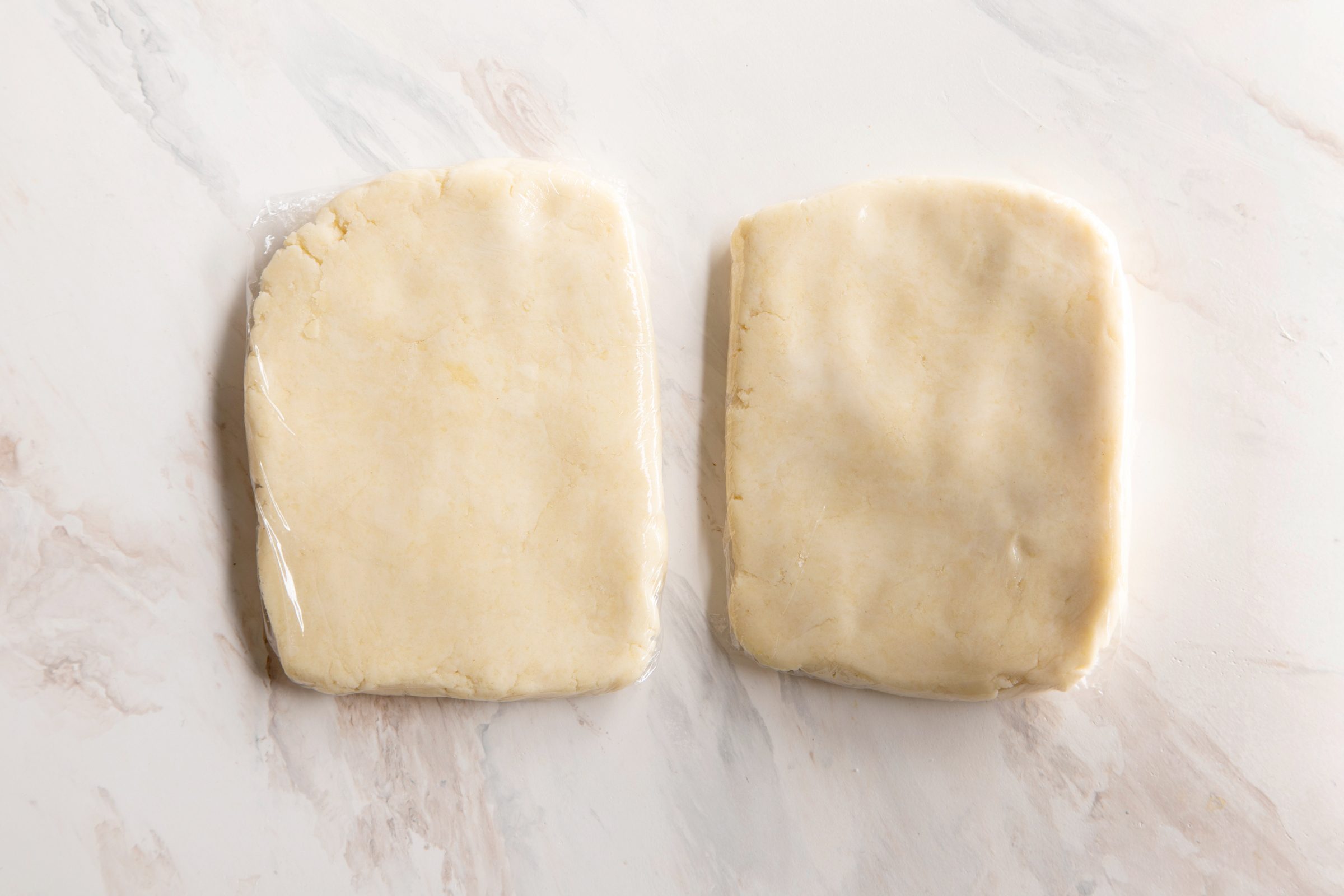 two pieces of dough wrapped in plastic wrap on the kitchen counter