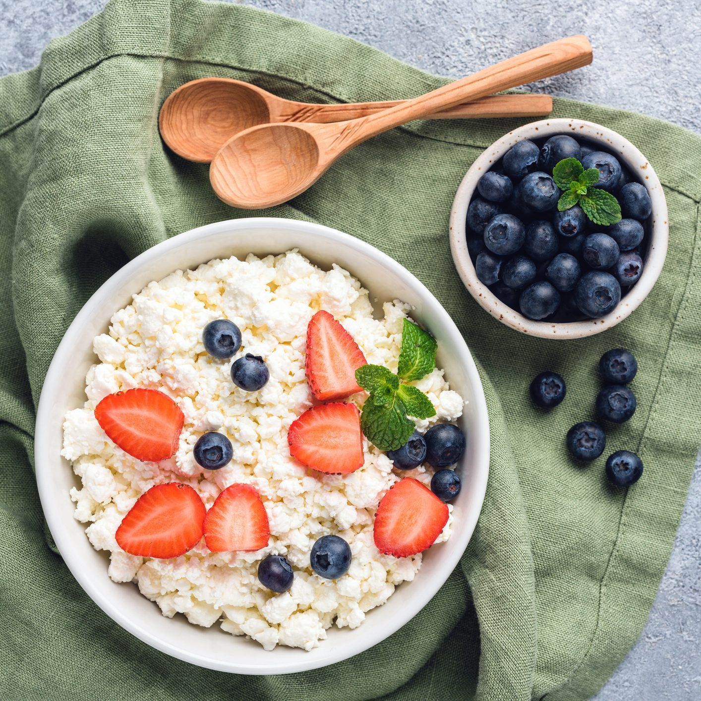 cottage cheese in a bowl with strawberries and blueberries with two wooden spoons to the side and another smaller bowl filled with blueberries