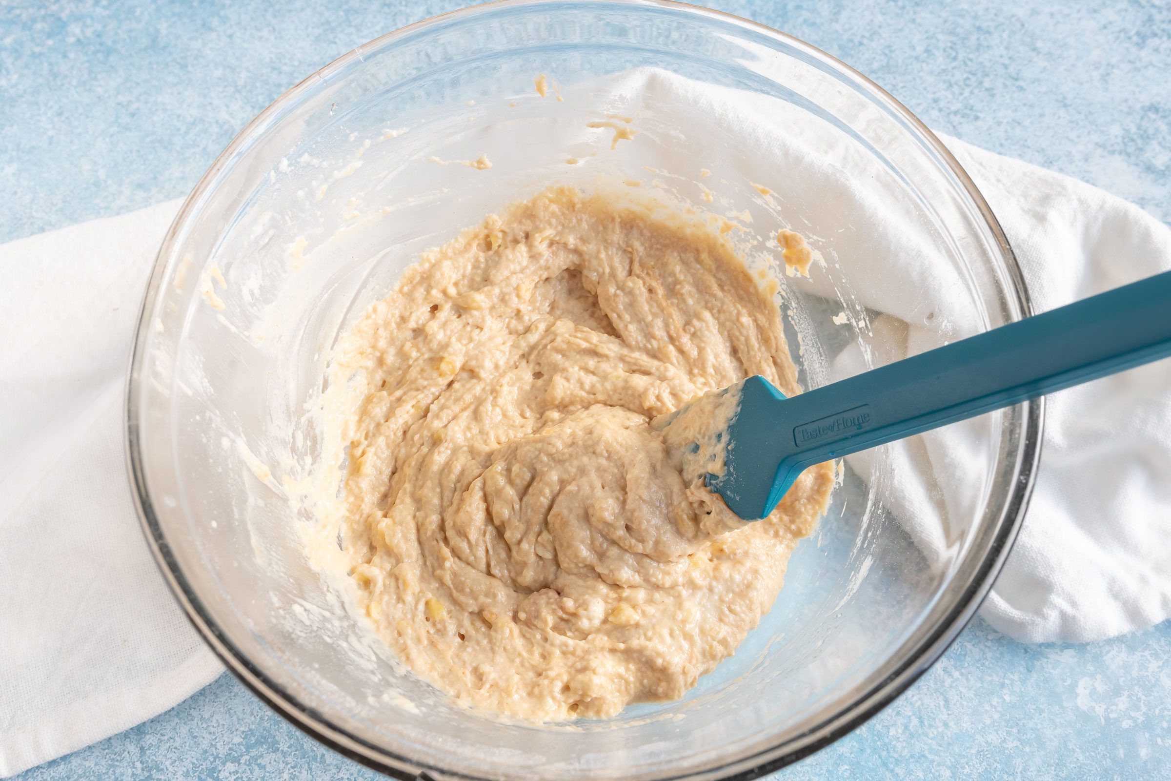 mixing batter for dog cupcakes a glass bowl with a rubber spatula on a blue countertop