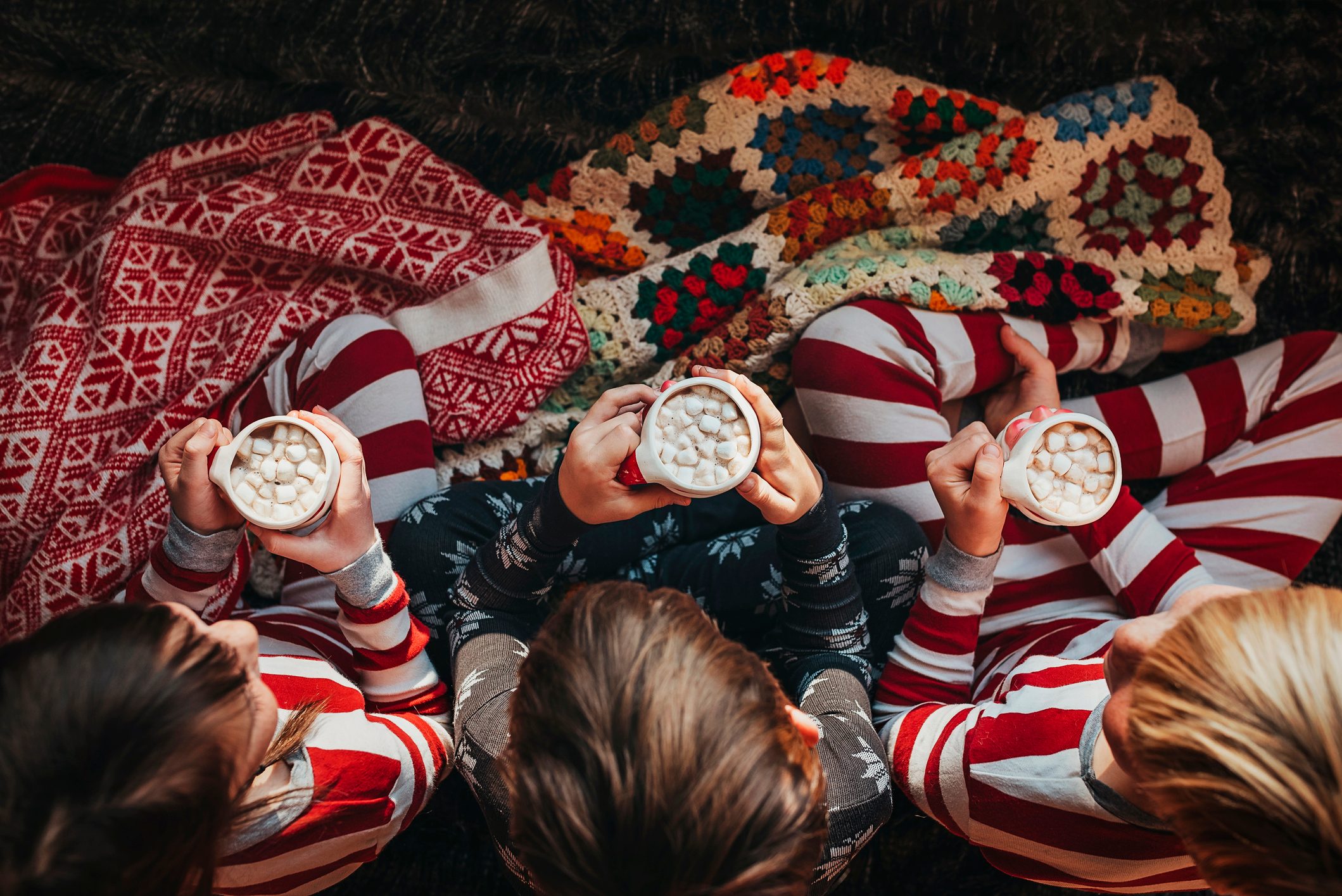 Three children sitting on a couch drinking hot chocolate