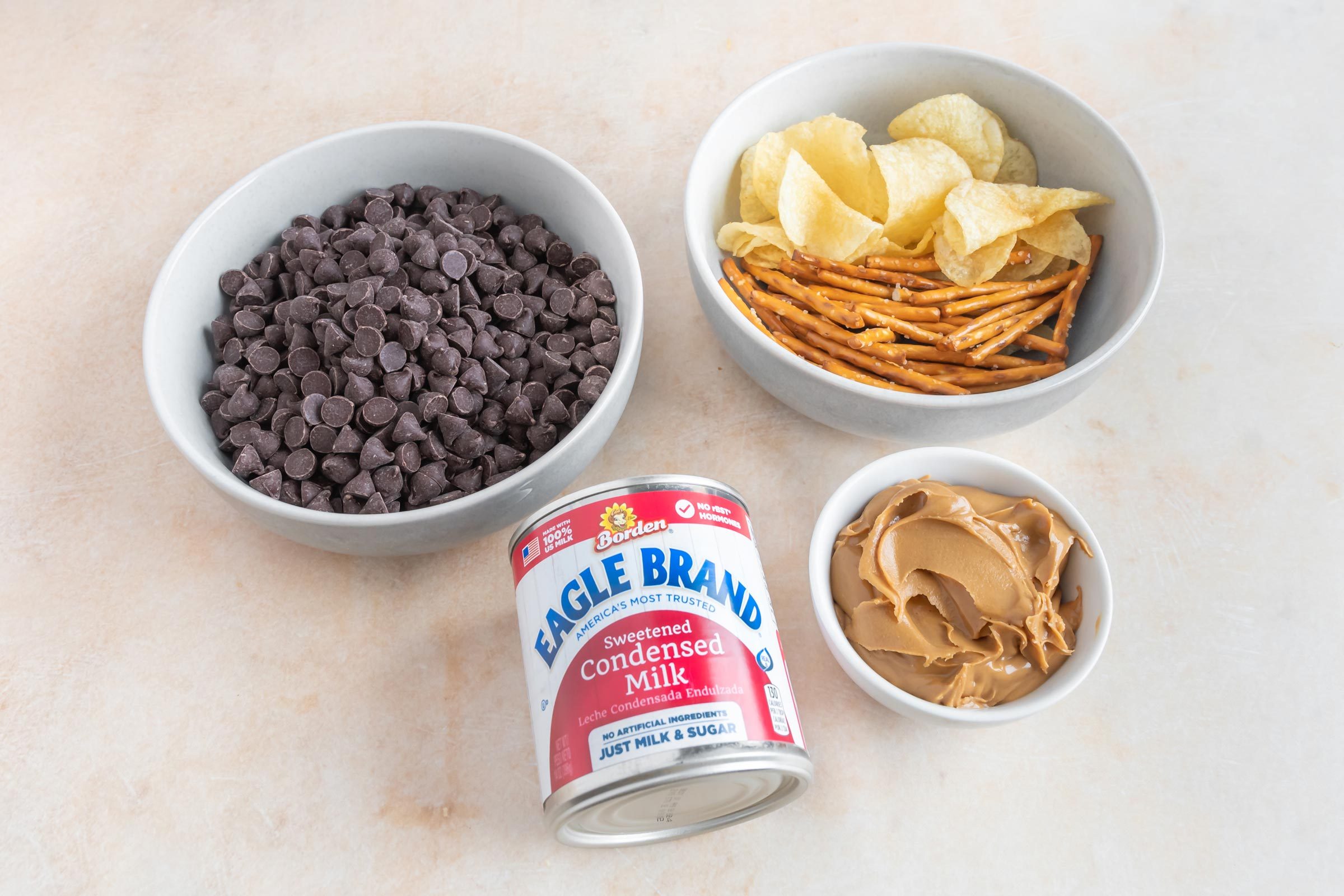 a bowl of chocolate chips, a bowl of peanut butter, a bowl of chips and a can of condensed milk