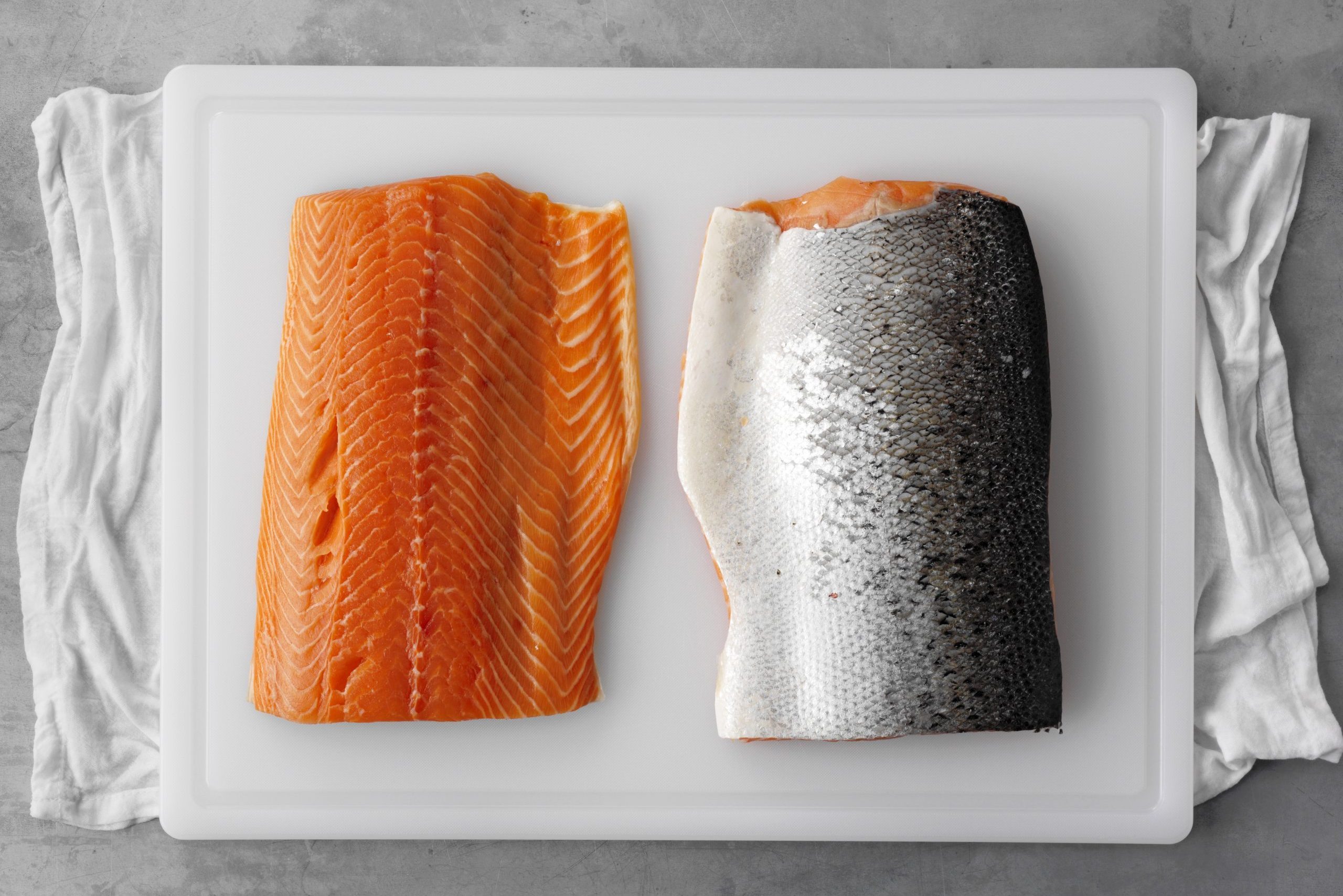 Prep sliced salmon on cutting board with one meat side up and the other skinside up while cutting board rests on a damp towel on the countertop