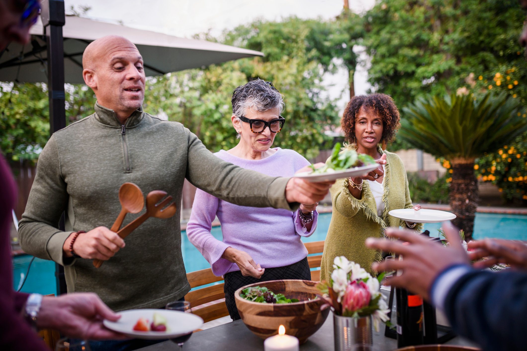 Man serving friends salad at backyard dinner party
