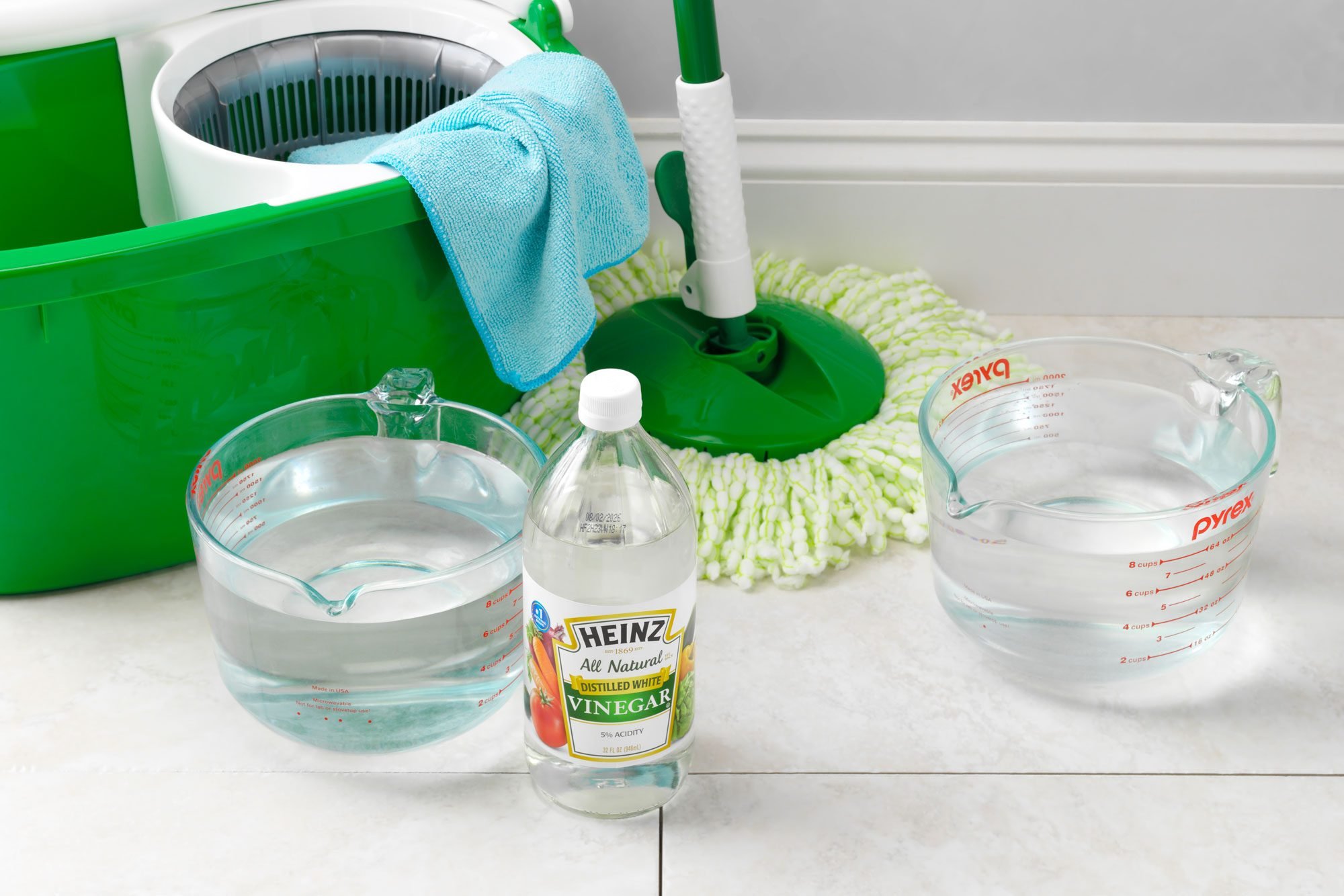 cleaning supplies for a homemade tile floor cleaner arranged on a tile floor near the wall