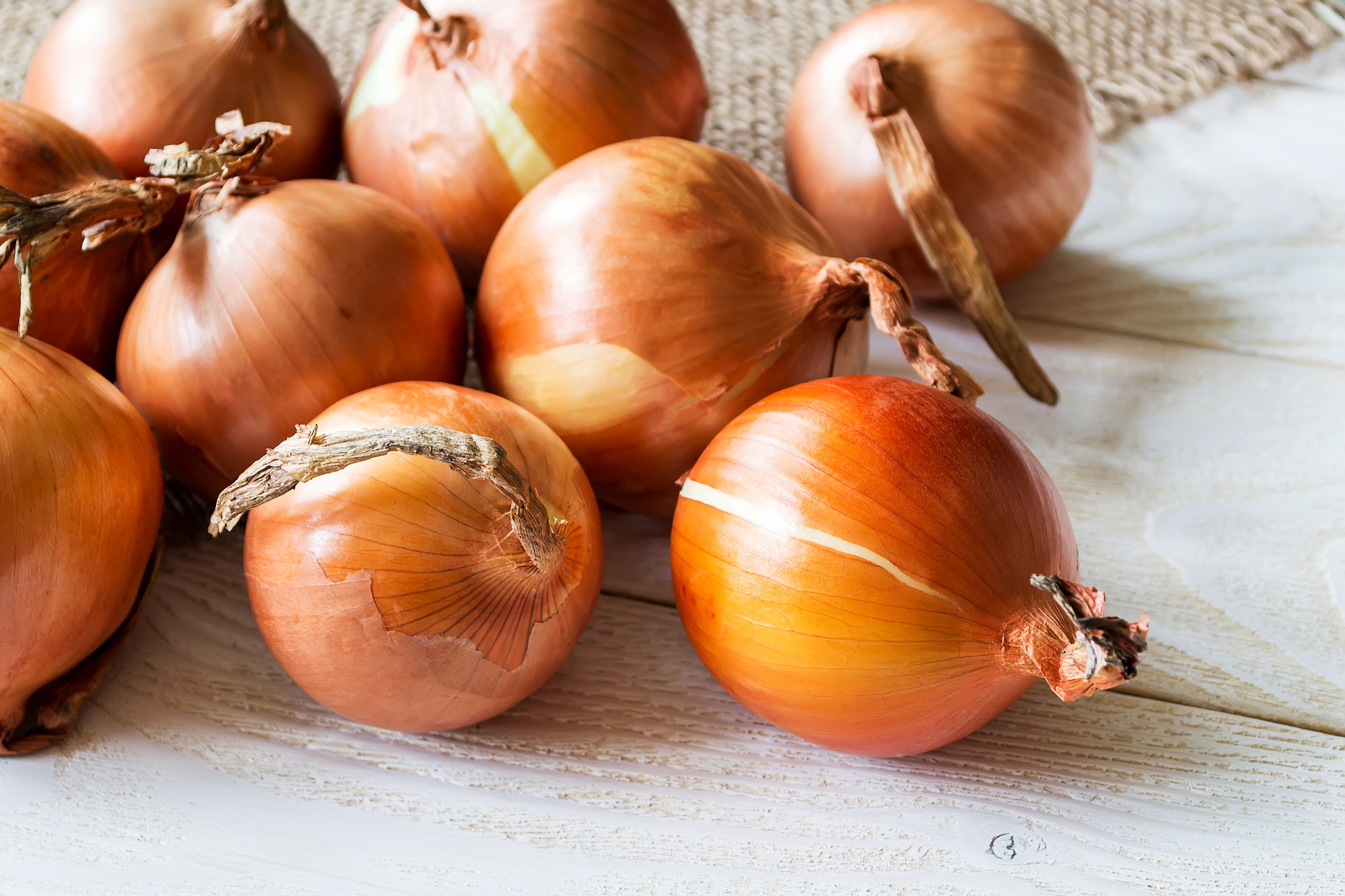 A lot of raw fresh yellow onions spilled out on a wooden rustic table. Vegetables, vegetarian and healthy eating. Food ingredients.