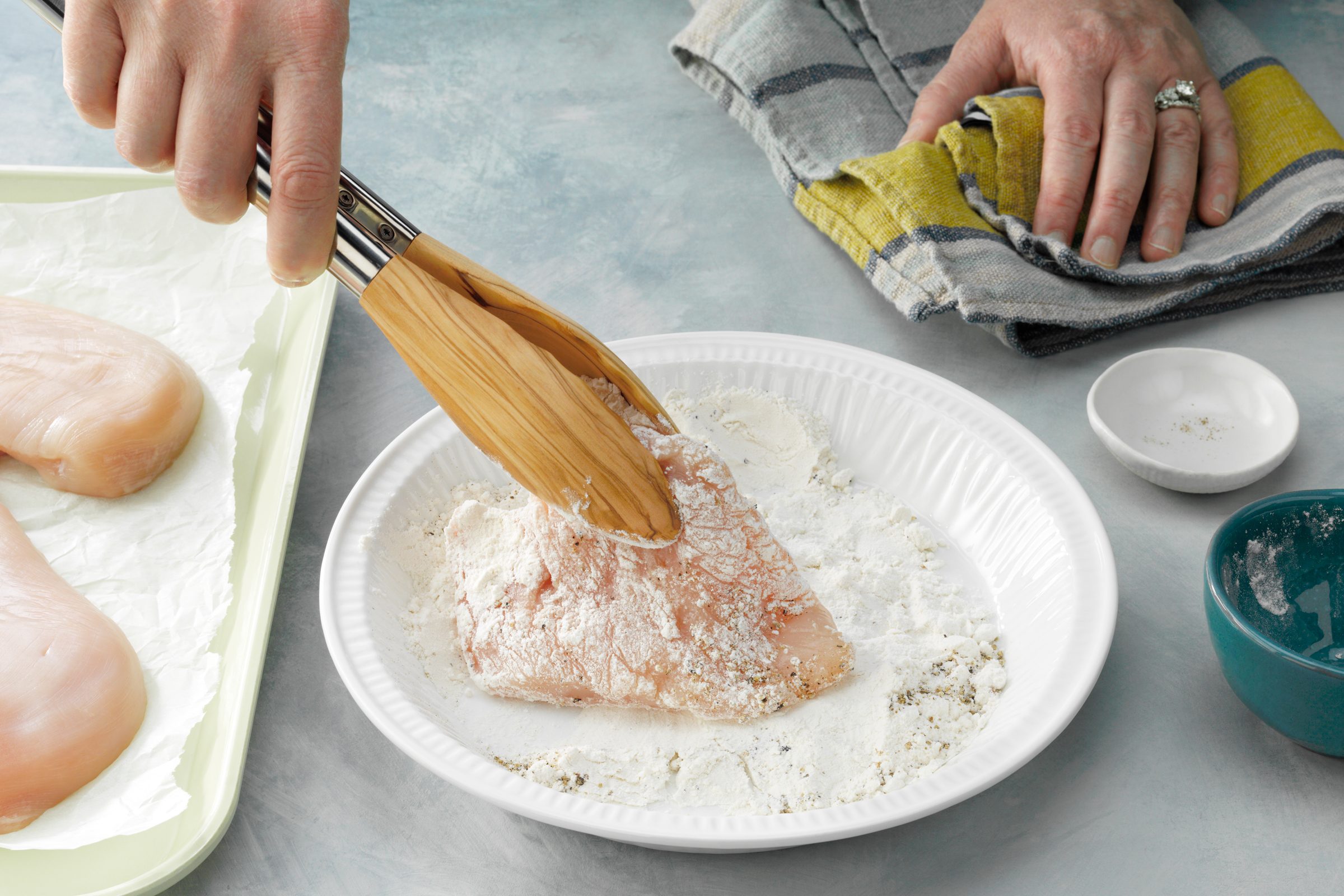 holding raw chicken with tongs and Dredging the chicken
