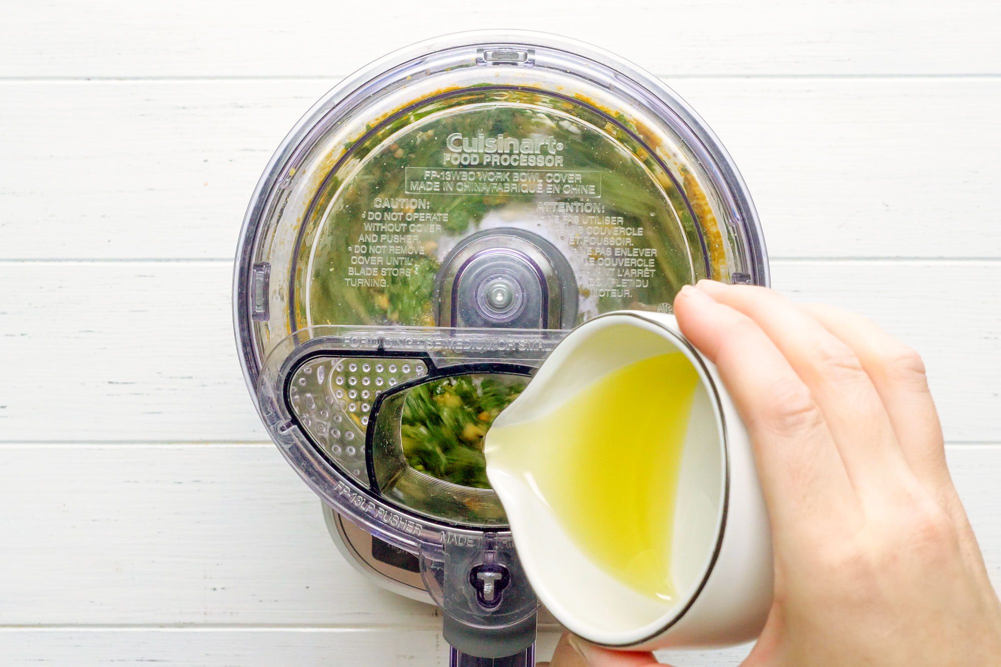 hand adding oil into food processor for vegan pesto