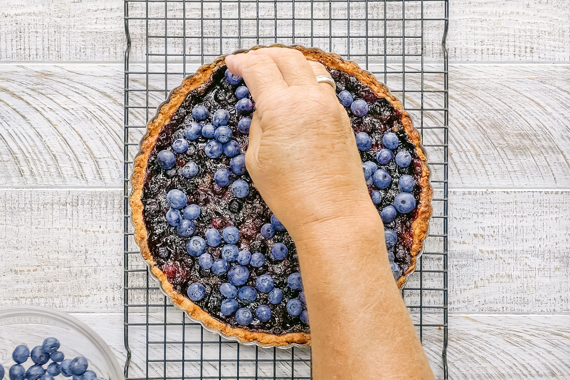 Topping Blueberries on Blueberry Tart on wire oven rack on wooden surface